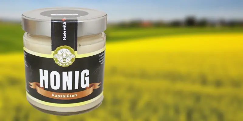 Rapshonig - Glas mit cremigem hellgelbem Rapshonig vom Imker vor gelbem Rapsfeld in Thüringen